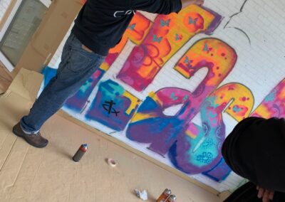 Mann steht vor einer weißen Wand und sprüht ein Graffitty-Bild