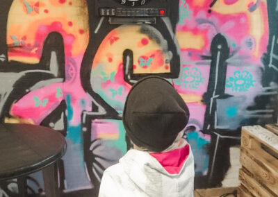 junges Mädchen spielt Darts auf einer Dartsscheibe, die an einer besprühten Graffitty-Wand hängt