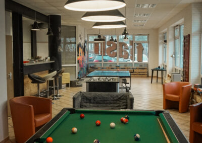 Billardtisch, Sessel, Tischfußball-Spiel, Tischtennisplatte und Bar in einem hell beleuchteten Raum